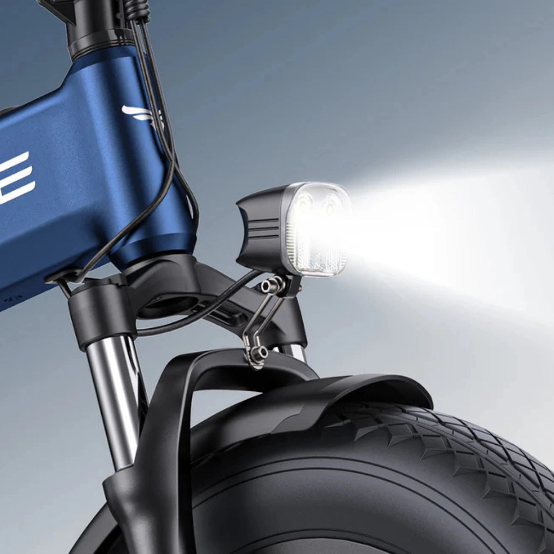 Izdelek na sliki je električno kolo, model Engwe Engine Pro 3.0 Boost. Na sliki je vidna sprednja luč, ki je pritrjena na okvir kolesa, ter del sprednjega kolesa z robustnim gumijastim profilom, kar nakazuje na njegovo zmogljivost in stabilnost. Kolo ima modro barvo okvirja in sodoben dizajn.