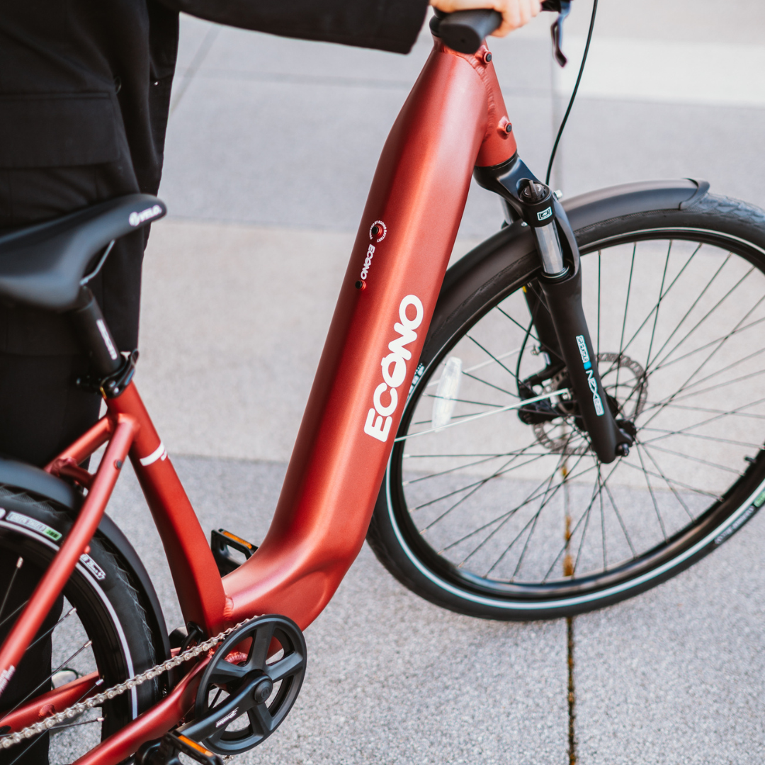Na sliki je električno kolo znamke Econo, model EER4. Kolo ima eleganten rdeč okvir in je opremljeno s sodobnimi komponentami. Vidna je tudi prednja vilica in del kolesa, kar nakazuje na njegovo urbano zasnovo, primerno za mestno vožnjo.