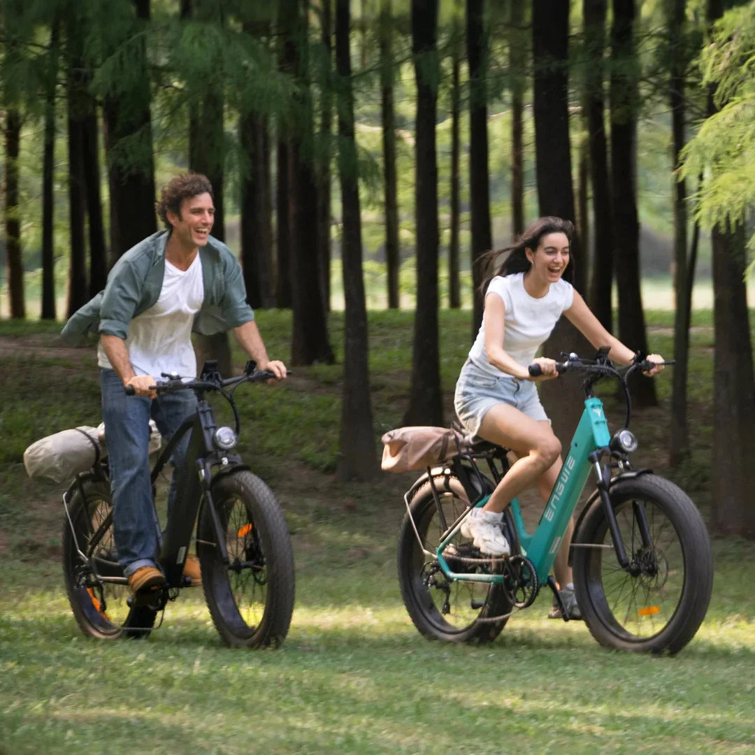 Izdelek na sliki je električno kolo, znamke Engwe, model E26. Na sliki sta prikazana moški in ženska, ki se zabavata med vožnjo po naravi. Obe kolesi imata široke pnevmatike in udobne sedeže, kar nakazuje na sproščeno in prijetno vožnjo. Okolica je gozdnata, kar ustvarja prijetno in naravno vzdušje.