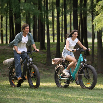 Izdelek na sliki je električno kolo, znamke Engwe, model E26. Na sliki sta prikazana moški in ženska, ki se zabavata med vožnjo po naravi. Obe kolesi imata široke pnevmatike in udobne sedeže, kar nakazuje na sproščeno in prijetno vožnjo. Okolica je gozdnata, kar ustvarja prijetno in naravno vzdušje.