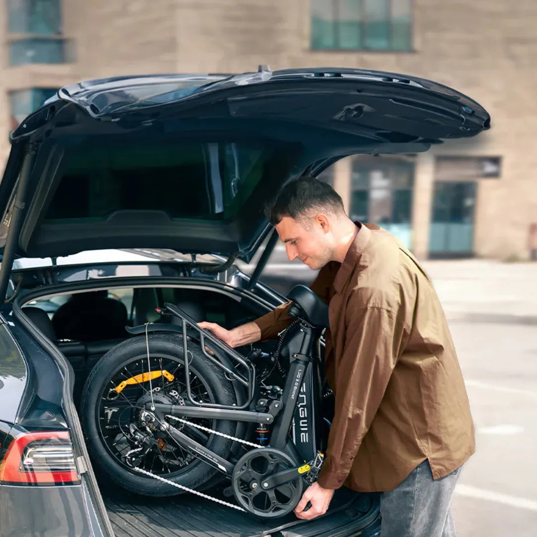 Na sliki je električno kolo znamke Engwe, model L20 3.0 Boost. Prikazano je v procesu nalaganja v prtljažnik avtomobila, kar nakazuje njegovo zložljivo zasnovo. Kolo ima kompaktno obliko in je opremljeno z manjšimi kolesi, kar olajša prenašanje in shranjevanje. Moški na sliki se zdi osredotočen na nalaganje kolesa, kar poudarja praktičnost izdelka.