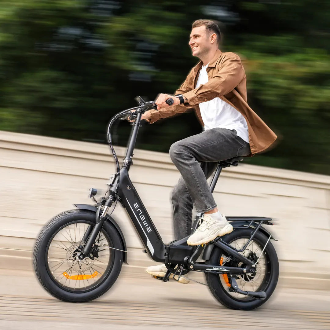Na sliki je električno kolo znamke Engwe, model L20. Kolo ima robustno konstrukcijo in široke pnevmatike, kar omogoča udobno vožnjo. Na sliki je prikazan moški, ki se vozi po cesti, oblečen v sproščeno obleko, kar nakazuje na sproščeno in prijetno izkušnjo vožnje. V ozadju so zelenje in arhitekturni elementi, kar dodaja dinamiko sceni.