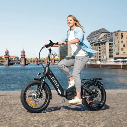 Izdelek je električno kolo znamke Engwe, model L20 3.0 Pro. Na sliki je vidna ženska, ki vozi kolo ob vodi, v ozadju pa so mestne zgradbe in most. Kolo ima široke pnevmatike in moderno obliko, kar nakazuje na udobno vožnjo. Oblečena je v sproščeno obleko, kar poudarja prijetno vzdušje vožnje.