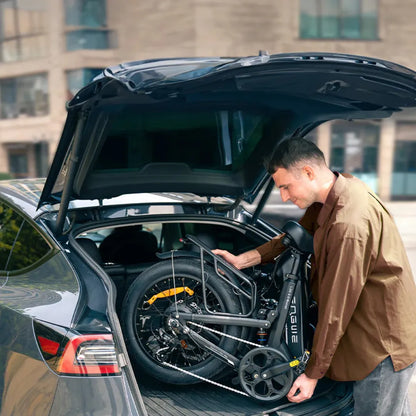 Na sliki je električno kolo znamke Engwe, model L20 3.0 Pro. Oseba na sliki je v procesu nalaganja zloženega kolesa v prtljažnik avtomobila. Kolo je kompaktno in zasnovano za enostavno prevoznost, kar je razvidno iz njegove zložljive oblike. V ozadju so vidne urbane zgradbe, kar nakazuje na mestno okolje.