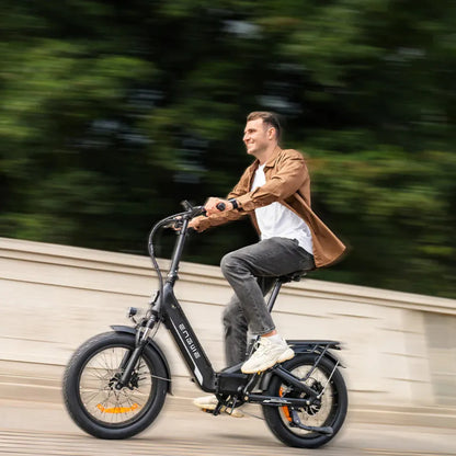 Izdelek na sliki je električno kolo, znamke Engwe, model L20 3.0 Pro. Na sliki je moški, ki se vozi na kolesu po cesti, obdanem z zelenjem. Kolo ima široka kolesa in moderno obliko, kar nakazuje na udobno vožnjo. Moški nosi sproščeno obleko in se zdi, da uživa v vožnji.