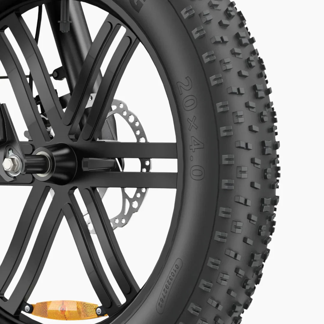 Izdelek je električno kolo, model Engwe L20 Boost. Na sliki je prikazan del sprednjega kolesa, ki ima široko gumo dimenzij 20x4.0, kar omogoča boljšo stabilnost in oprijem na različnih terenih. Vidna je tudi diskasta zavora in del kolesa, ki je oblikovan s petimi kraki. Guma ima izrazit profil, kar je primerno za vožnjo po zahtevnejših površinah.