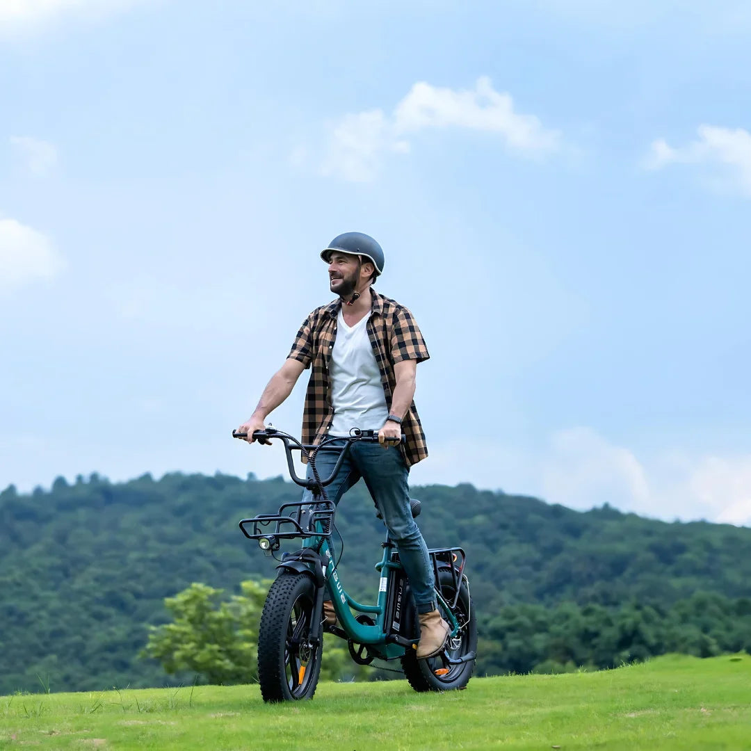 Izdelek na sliki je električno kolo, model Engwe L20 Boost. Na sliki je moški, ki se vozi po travnati površini, oblečen v sproščeno obleko in čelado. Kolo ima široke pnevmatike, kar nakazuje na dobro stabilnost in udobje pri vožnji po različnih terenih. V ozadju so zelene hribe in modro nebo, kar ustvarja prijetno naravno okolje.