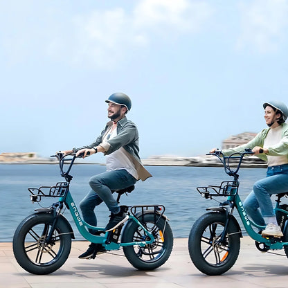 Na sliki je električno kolo znamke Engwe, model L20 Boost. Kolo ima široke pnevmatike in je zasnovano za udobno vožnjo. Dva kolesarja, moški in ženska, se peljeta ob obali, oblečena sta v sproščena oblačila in nosita čelade. V ozadju je vidna morska panorama, kar ustvarja prijetno vzdušje za vožnjo.
