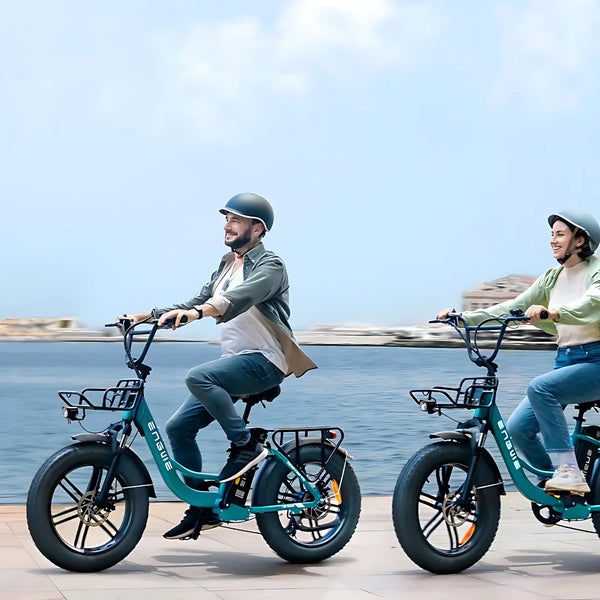 Na sliki je električno kolo znamke Engwe, model L20 Boost. Kolo ima široke pnevmatike in je zasnovano za udobno vožnjo. Dva kolesarja, moški in ženska, se peljeta ob obali, oblečena sta v sproščena oblačila in nosita čelade. V ozadju je vidna morska panorama, kar ustvarja prijetno vzdušje za vožnjo.