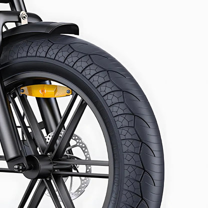 Izdelek na sliki je električno kolo, model Engwe M1. Na sliki je prikazan del sprednjega kolesa, ki vključuje široko pnevmatiko z izrazitim profilom, kar nakazuje na dobro oprijemljivost. Vidna je tudi zavora in del okvirja, kar kaže na robustno zasnovo kolesa.