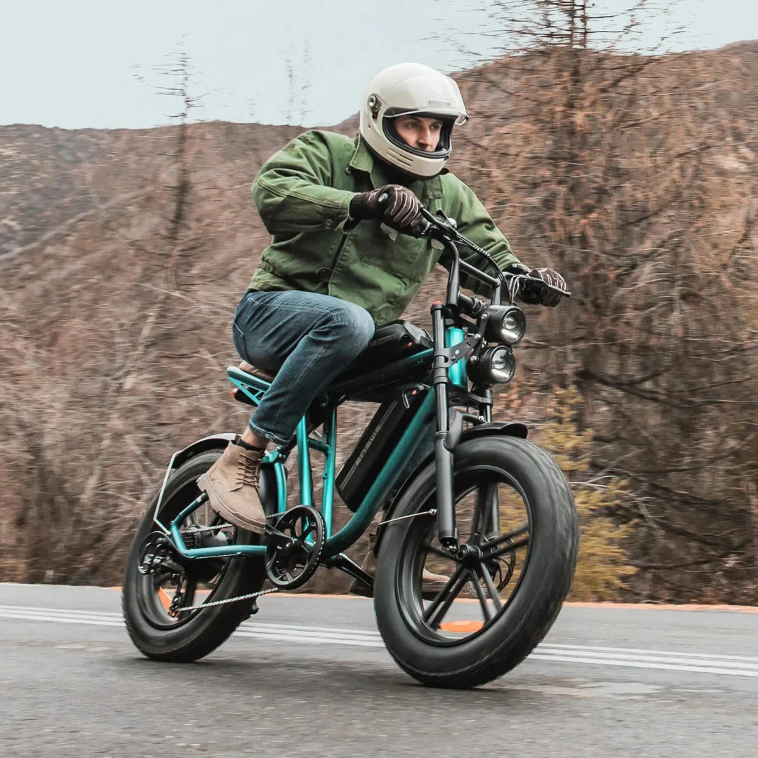 Na sliki je električno kolo znamke Engwe, model M20. Kolo je zasnovano za vožnjo po različnih terenih, opremljeno je z močnimi pnevmatikami in dvema sprednjima lučema. Na kolesu se vozi moški, oblečen v zaščitno čelado in jakno, kar nakazuje na aktivno in dinamično vožnjo. V ozadju so vidne naravne pokrajine, kar dodatno poudarja avanturistični duh vožnje.