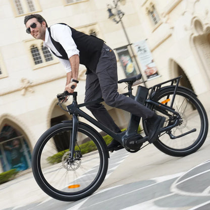 Izdelek je električno kolo znamke Engwe, model P275 Pro. Na sliki je moški, oblečen v elegantno obleko, ki se vozi na temnem električnem kolesu. Kolo ima široke pnevmatike in opremo za udobno vožnjo, vidna pa je tudi baterija na okvirju. Ozadje prikazuje arhitekturne elemente in mestno okolje.