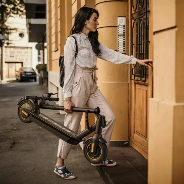 Ženska, ki nosi električni skiro Engwe Y10, se približuje vratom v mestnem okolju.
