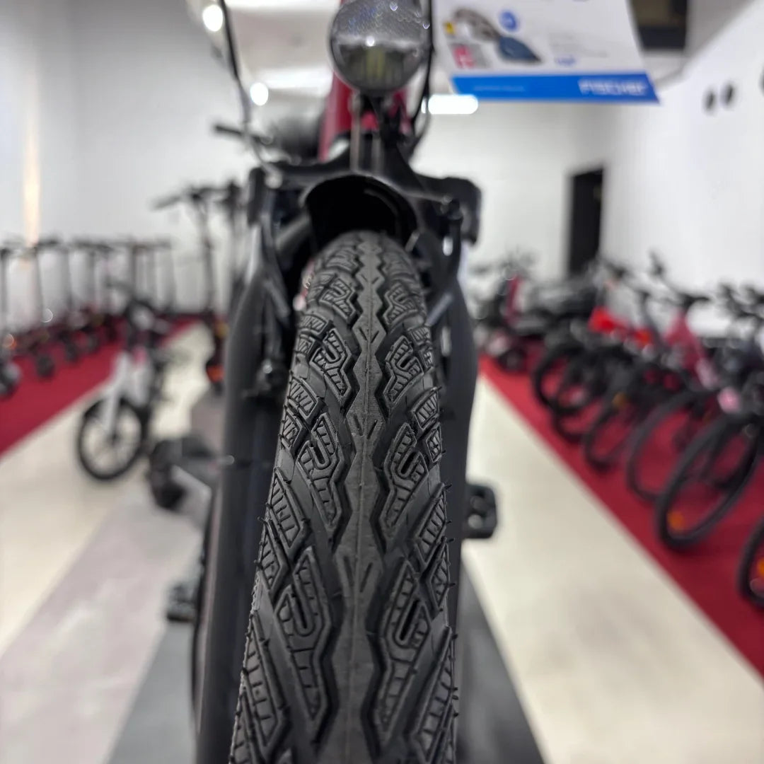 Na sliki je električno kolo znamke Fischer, model Cita 1.0. Vidna je sprednja pnevmatika z značilnim vzorcem, ki omogoča dober oprijem. V ozadju so vidni tudi drugi kolesi v trgovini, kar nakazuje, da gre za prodajni prostor.