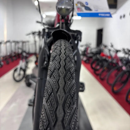 Na sliki je električno kolo znamke Fischer, model Cita 1.0. Vidna je sprednja pnevmatika z značilnim vzorcem, ki omogoča dober oprijem. V ozadju so vidni tudi drugi kolesi v trgovini, kar nakazuje, da gre za prodajni prostor.