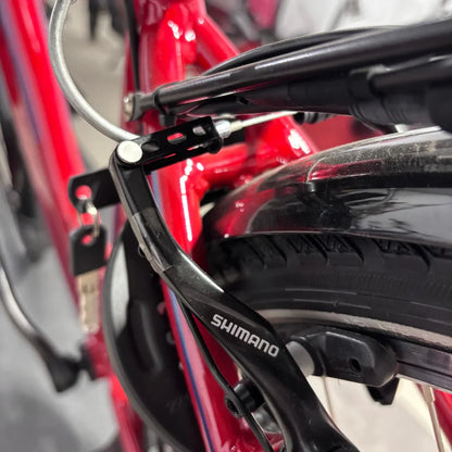 Izdelek na sliki je električno kolo znamke Fischer, model Cita 1.0. Na sliki je vidna del kolesa, vključno z zavorami in delom okvirja. Zavorni sistem je označen z logotipom Shimano, kar nakazuje na kakovostne komponente. Kolo je v rdeči barvi, kar mu daje privlačen videz.