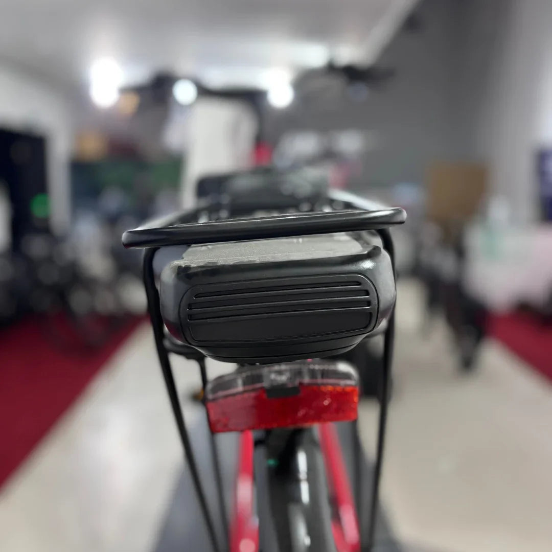 Izdelek je električno kolo znamke Fischer, model Cita 1.0. Na sliki je vidna zadnja stran kolesa, kjer je nameščen akumulator ter nosilec za prtljago. V ozadju so vidni drugi kolesi in del trgovine, kar nakazuje, da gre za prodajno okolje.