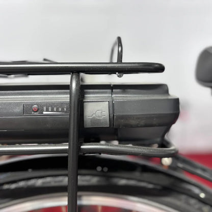 Na sliki je električno kolo znamke Fischer, model Cita 1.0. Vidna je baterija, nameščena na zadnjem nosilcu, z gumbom za vklop in indikatorjem napolnjenosti. Baterija ima tudi priključek za polnjenje, kar nakazuje na električni sistem kolesa.