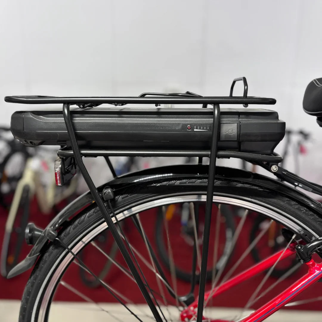 Izdelek na sliki je električno kolo znamke Fischer, model Cita 1.0. Na sliki je prikazan del kolesa s pritrjenim akumulatorjem, ki je nameščen na zadnjem nosilcu. Kolo ima rdečo barvo in je opremljeno s širokimi gumami. V ozadju so vidni tudi drugi kolesi.