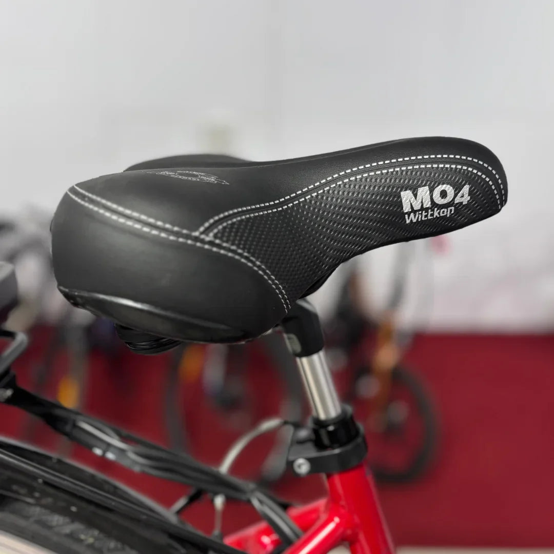 Izdelek na sliki je električno kolo znamke Fischer, model Cita 1.0. Na sliki je prikazano sedežno blato, ki je črne barve in ima oznako MO4 ter blagovno znamko Wittkop. Kolo je v rdeči barvi, v ozadju pa so vidni drugi kolesi.