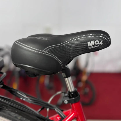 Izdelek na sliki je električno kolo znamke Fischer, model Cita 1.0. Na sliki je prikazano sedežno blato, ki je črne barve in ima oznako MO4 ter blagovno znamko Wittkop. Kolo je v rdeči barvi, v ozadju pa so vidni drugi kolesi.