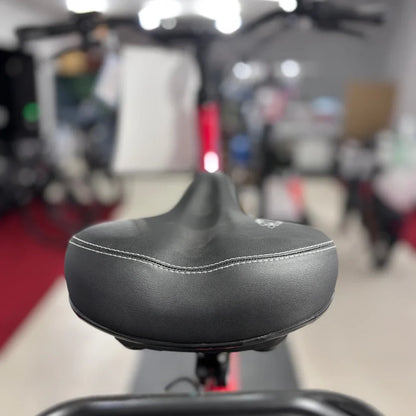 Izdelek je električno kolo znamke Fischer, model Cita 1.0. Na sliki je vidna sedežna blazina kolesa, ki je črne barve in ima bele šive. V ozadju je del okvirja kolesa, kar nakazuje na njegovo zasnovo in stil.