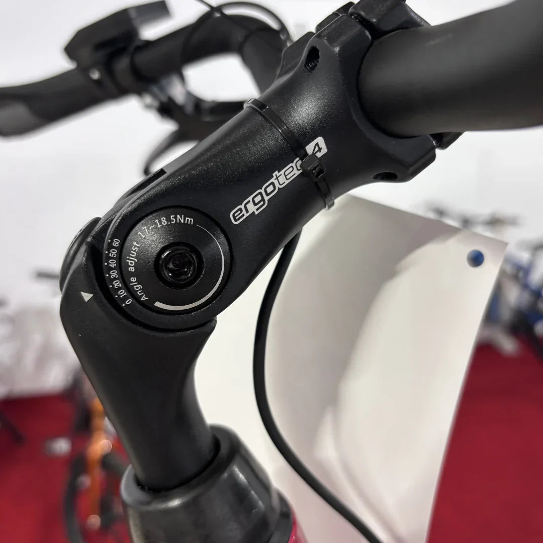 Izdelek je električno kolo, znamke Fischer, model Cita 1.0. Na sliki je prikazan del krmila, kjer je vidna nastavljiva povezava z oznako "ergotec". Ta del omogoča prilagoditev kota krmila, kar prispeva k udobnejši vožnji. V ozadju so delno vidni tudi drugi kolesi.