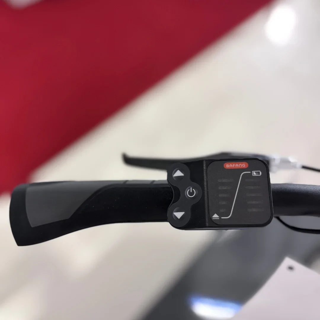 Izdelek je električno kolo znamke Fischer, model Cita 1.0. Na sliki je prikazan del krmila, kjer so vidni gumbi za upravljanje, vključno s stikalom za vklop in indikatorjem delovanja. Opremljeno je z električnim motorjem Bafang, kar nakazuje na njegovo funkcionalnost in zmogljivost pri vožnji.