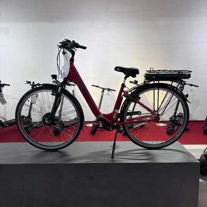 Na sliki je električno kolo znamke Fischer, model Cita 1.0. Kolo je rdeče barve in ima udoben okvir z nizkim prečnim članom, kar olajša vstopanje. Na zadnjem delu kolesa je nameščena baterija, kar nakazuje na njegovo električno delovanje. V ozadju so vidni tudi drugi električni skiroji, kar daje občutek o raznolikosti električnih prevoznih sredstev.