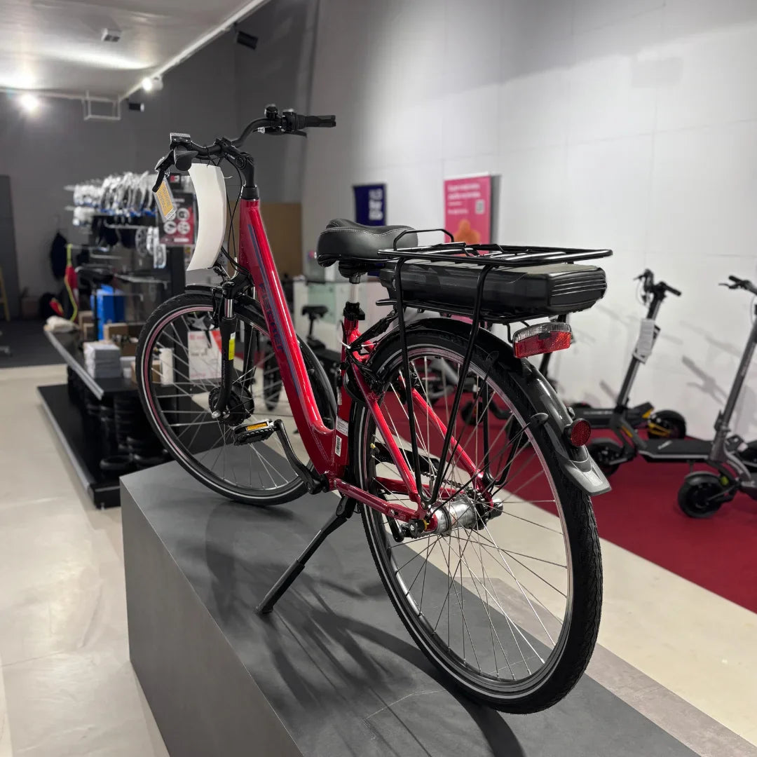 Izdelek na sliki je električno kolo, znamke Fischer, model Cita 1.0. Na sliki je vidno rdeče električno kolo, ki ima nameščen akumulator na zadnjem delu okvirja. Kolo je postavljeno na stojalo v trgovini, v ozadju pa so vidni tudi drugi izdelki, kot so električni skiroji.