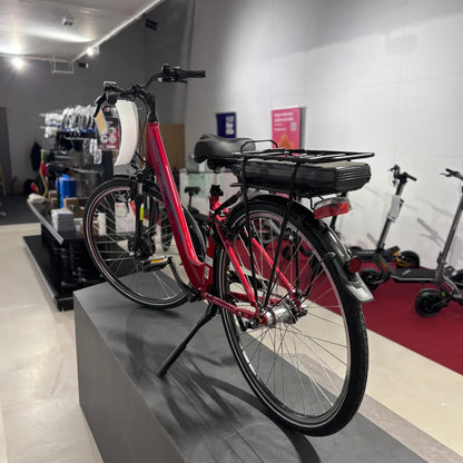 Izdelek na sliki je električno kolo, znamke Fischer, model Cita 1.0. Na sliki je vidno rdeče električno kolo, ki ima nameščen akumulator na zadnjem delu okvirja. Kolo je postavljeno na stojalo v trgovini, v ozadju pa so vidni tudi drugi izdelki, kot so električni skiroji.