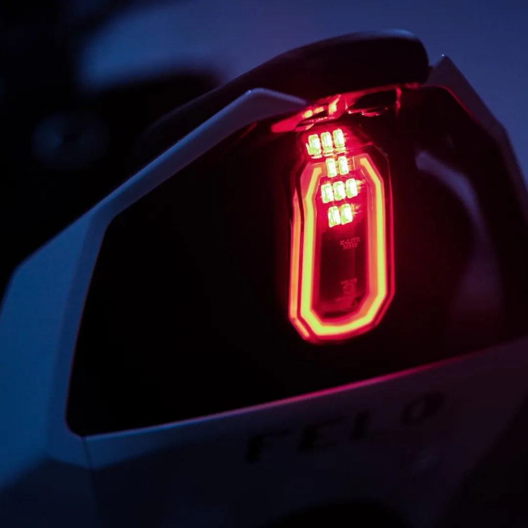 Od blizu posnet zadnji luči električnega skuterja Felo Fw 06, ki v šibki svetlobi žari rdeče.