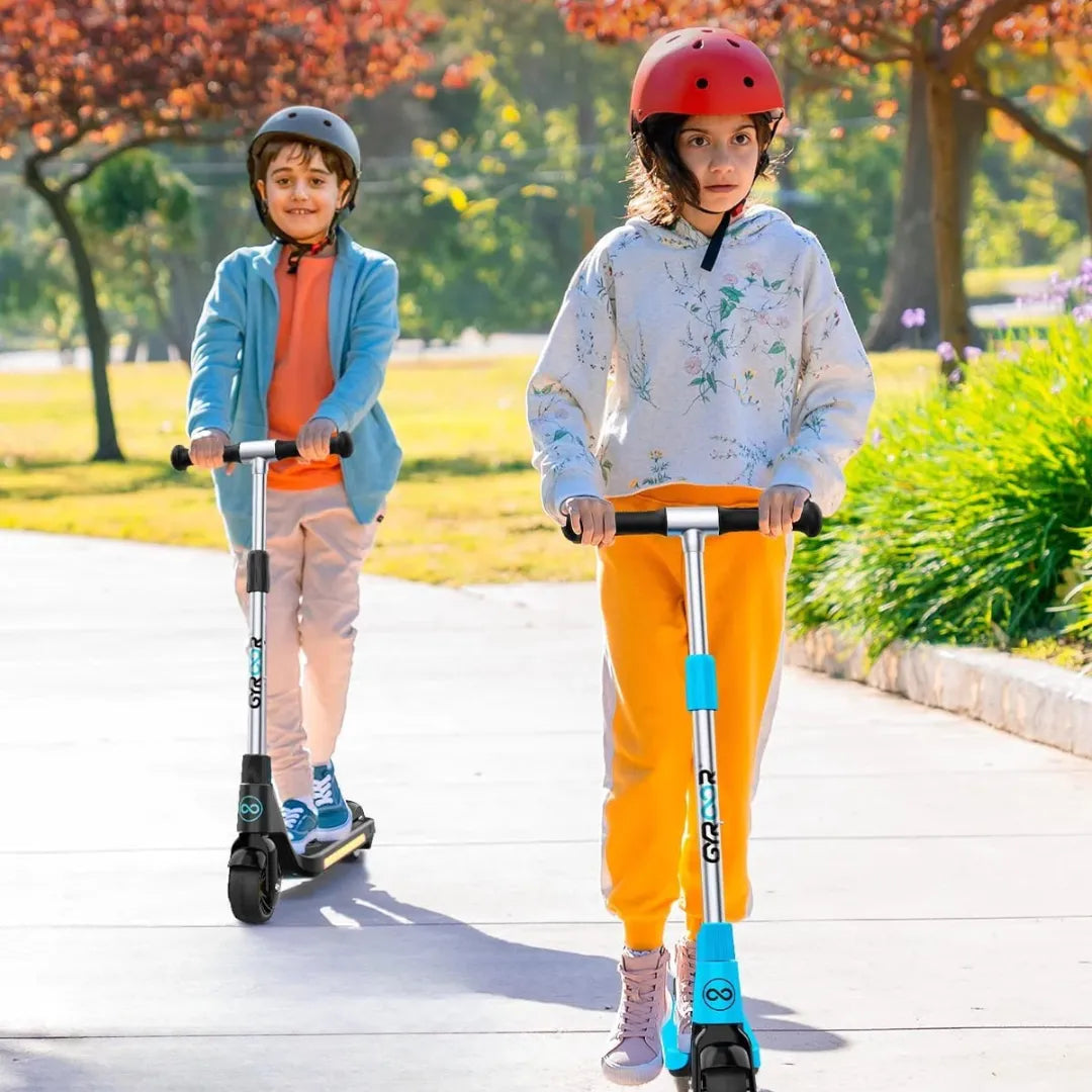 Na sliki je prikazan električni skiro, model Gyroor H30. Vidimo dva otroka, ki se vozita na skirojih po sprehajalni poti v parku. Oba nosita čelade za zaščito, eden je oblečen v svetlo modro jakno, drugi pa v sivo majico in oranžne hlače. V ozadju so drevesa in cvetje, kar ustvarja prijetno naravno okolje.