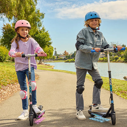 Izdelek je električni skiro, model Gyroor H30 Max. Na sliki sta vidna dva otroka, ki se vozita na skirojih ob obrežju, oblečena sta v zaščitno opremo, vključno s čeladami in zaščitnimi koleni. Okolica je zelena, ob vodi, kar ustvarja prijetno vzdušje za vožnjo.