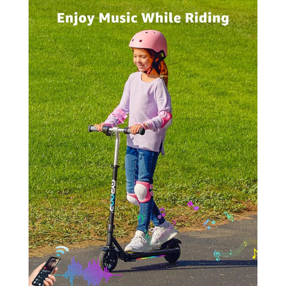 Na sliki je električni skiro, model Gyroor H30 Max. Vidimo deklico, ki se vozi na skiroju, oblečeno v udobna oblačila in zaščitno opremo, vključno s čelado in zaščitami za kolena. Ozadje prikazuje zeleno travo, kar ustvarja prijetno in igrivo vzdušje. Besedilo na sliki sporoča, da lahko uživate v glasbi med vožnjo.