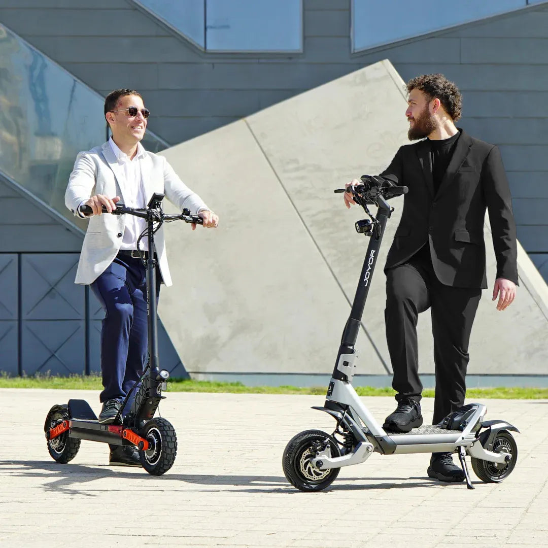 Moška v oblekah se vozita z električnim skirojem Joyor Luxerider in se smehljata zunaj v modernem okolju.
