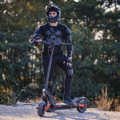 Na sliki je električni skiro, model Joyor S5 Z. Oseba na skiroju nosi zaščitno opremo, vključno s čelado in zaščitnimi blazinicami, kar nakazuje na aktivno in varno uporabo skiroja. Ozadje prikazuje naravno okolje, kar lahko pomeni, da je skiro primeren za vožnjo po različnih terenih.