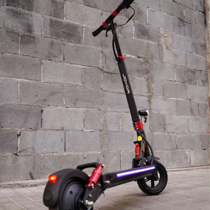 Na sliki je električni skiro, model Joyor G5. Izdelek je črne barve z rdečimi detajli in ima sodoben dizajn. Vidna sta tudi LED lučka na zadnjem delu skiroja ter krmilo, kar nakazuje na funkcionalnost in uporabnost v urbanem okolju. Ozadje slike je zid iz betonskih blokov, kar daje industrijski videz.