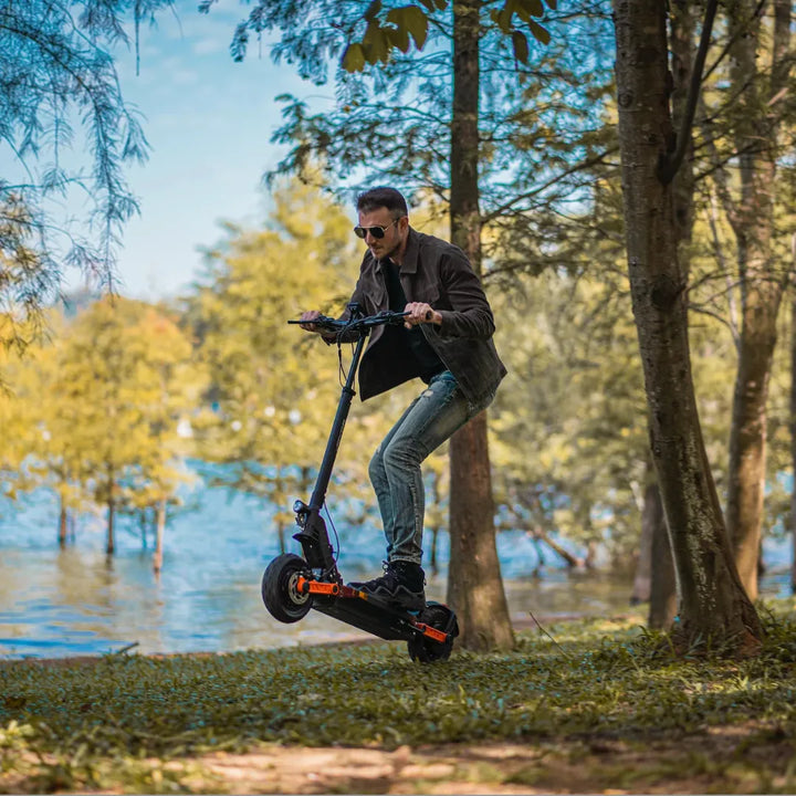 Oseba, ki vozi električni skiro Joyor S10 S Z, skače čez travnato površino ob jezeru.