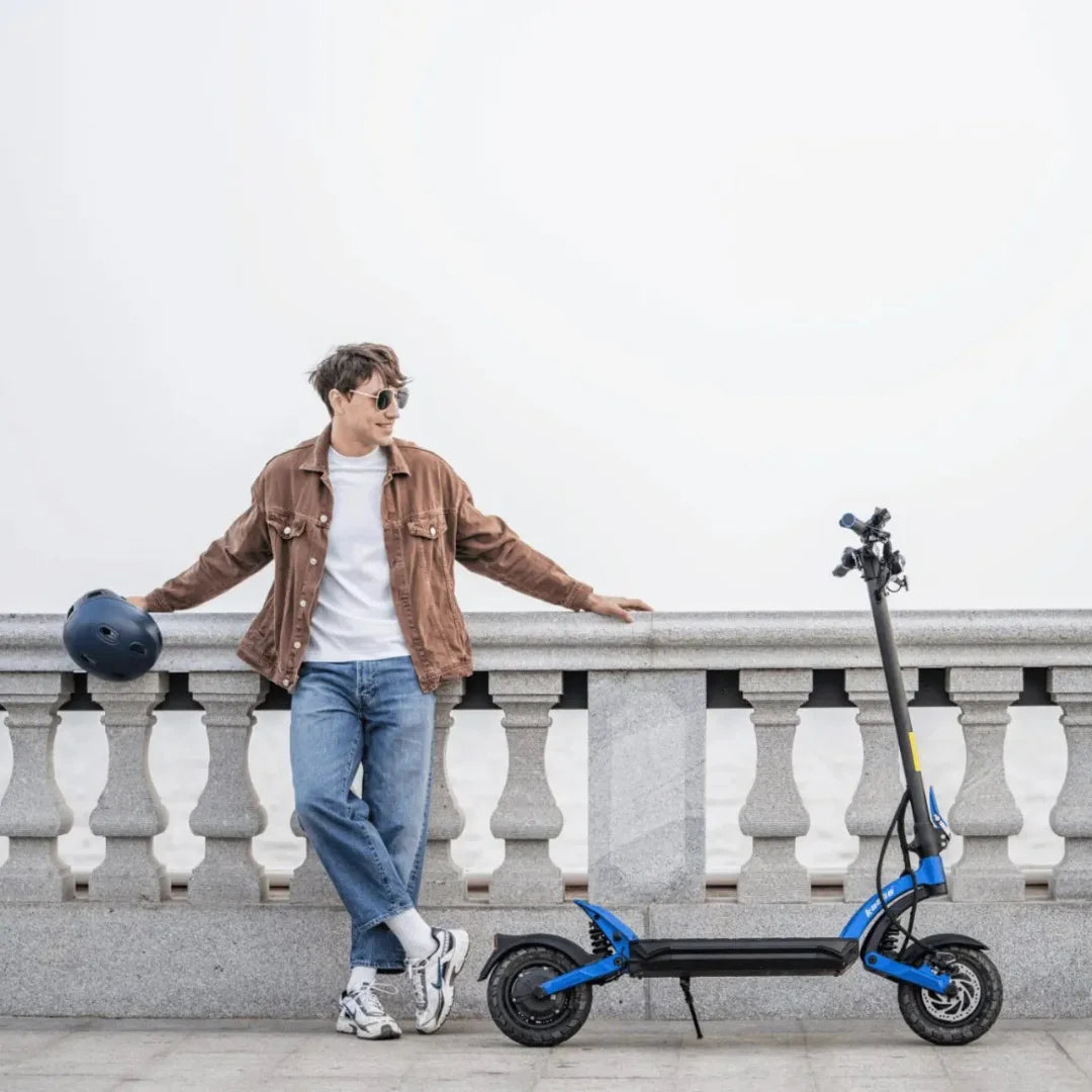 Oseba se naslanja na ograjo poleg električnega skiroja Kaabo Mantis X Plus.