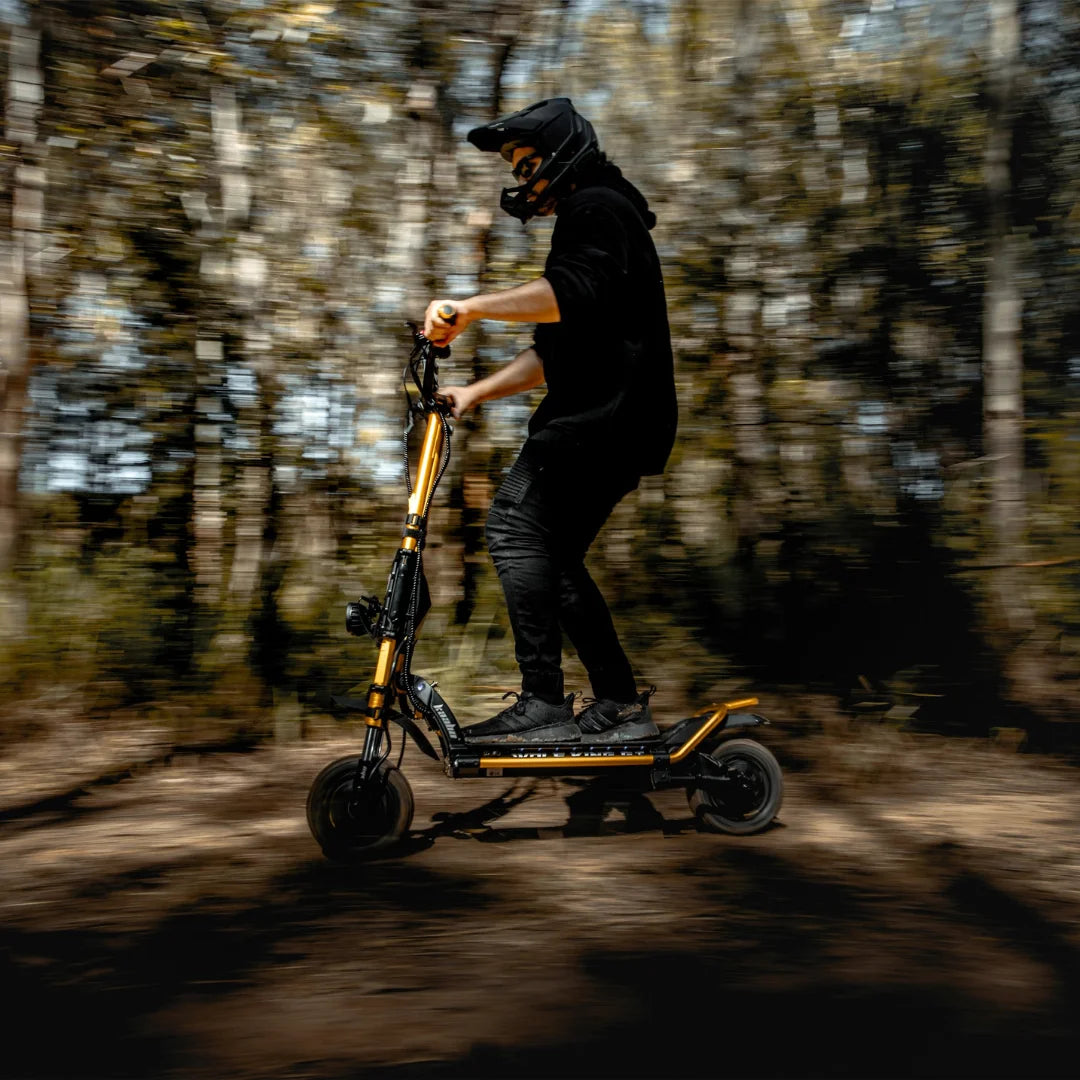 Voznik s čelado manevrira z električnim skirojem Kaabo Wolf King GT Pro skozi gozd.