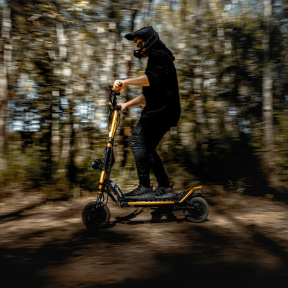 Voznik s čelado manevrira z električnim skirojem Kaabo Wolf King GT Pro skozi gozd.