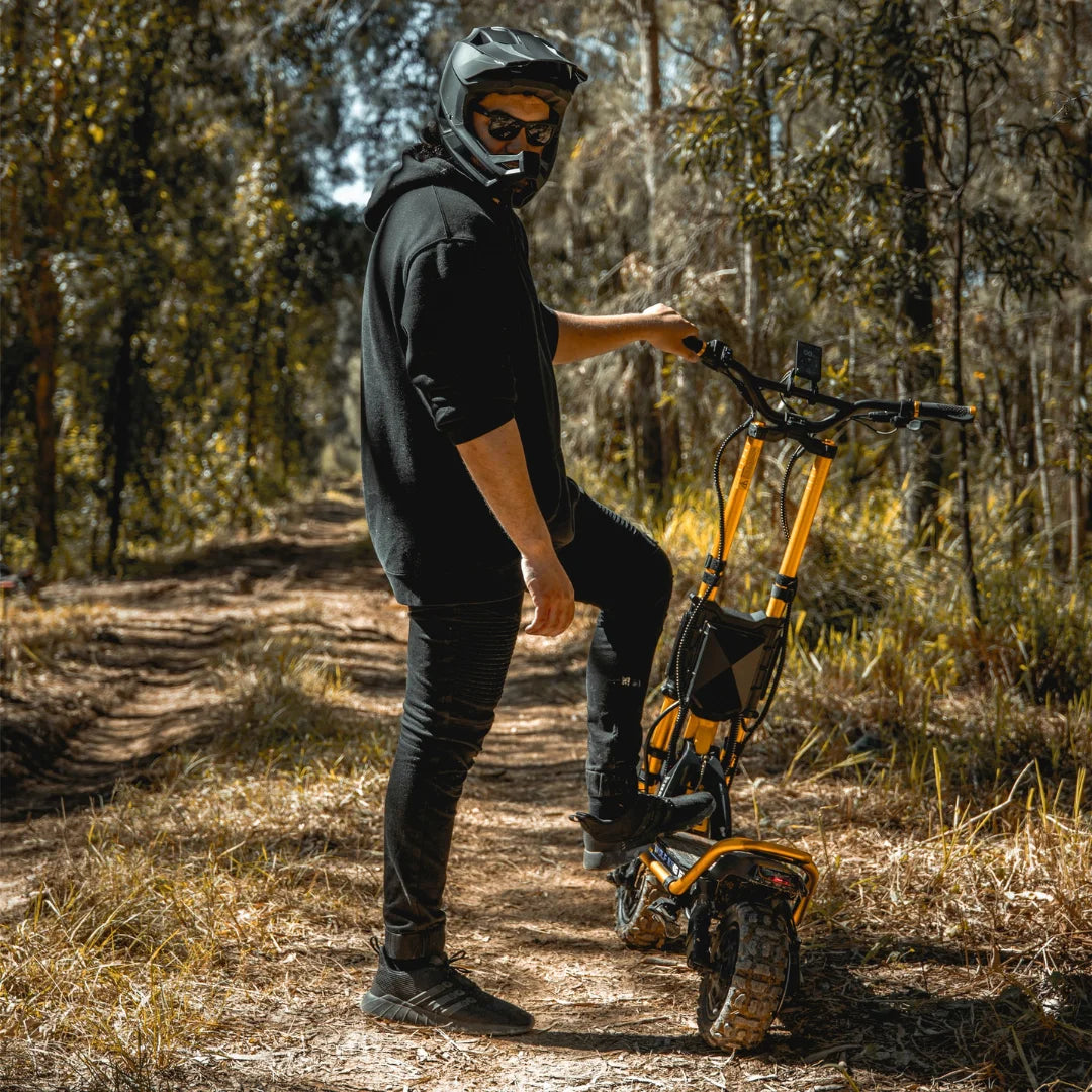 Oseba s čelado stoji ob električnem skiroju Kaabo Wolf King GT Pro na gozdni poti.