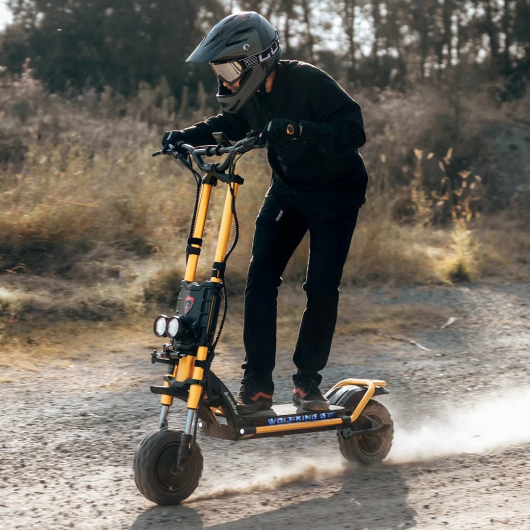 Jezdec s čelado se hitro vozi z električnim skirojem Kaabo Wolf King GT Pro po makadamski poti.