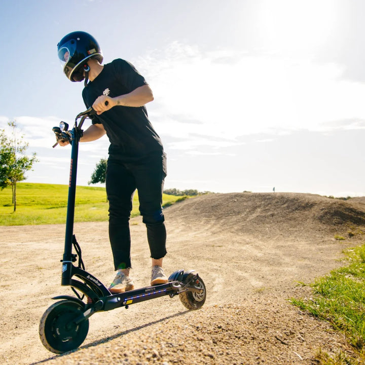 Oseba se vozi z električnim skirojem Kaabo Mantis 10 Plus po makadamski poti v sončnem parku.