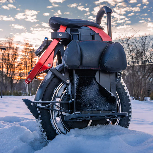 Izdelek na sliki je električni monocikel, model Kingsong S22 Pro. Na sliki je prikazan zadnji del monocikla, ki ima široko pnevmatiko in udobno sedežno površino. V ozadju se vidi zasnežena pokrajina in sončni zahod, kar ustvarja slikovit ambient. Monocikel je opremljen s sistemom za vzmetenje, kar nakazuje na udobno vožnjo.