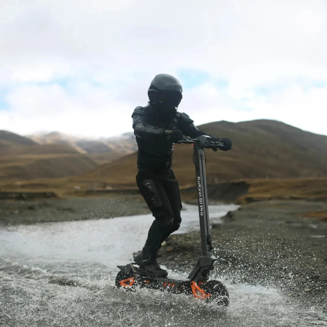 Voznik električnega skiroja Kukirin G1 Pro drsi skozi plitvo vodo v razgibani pokrajini.