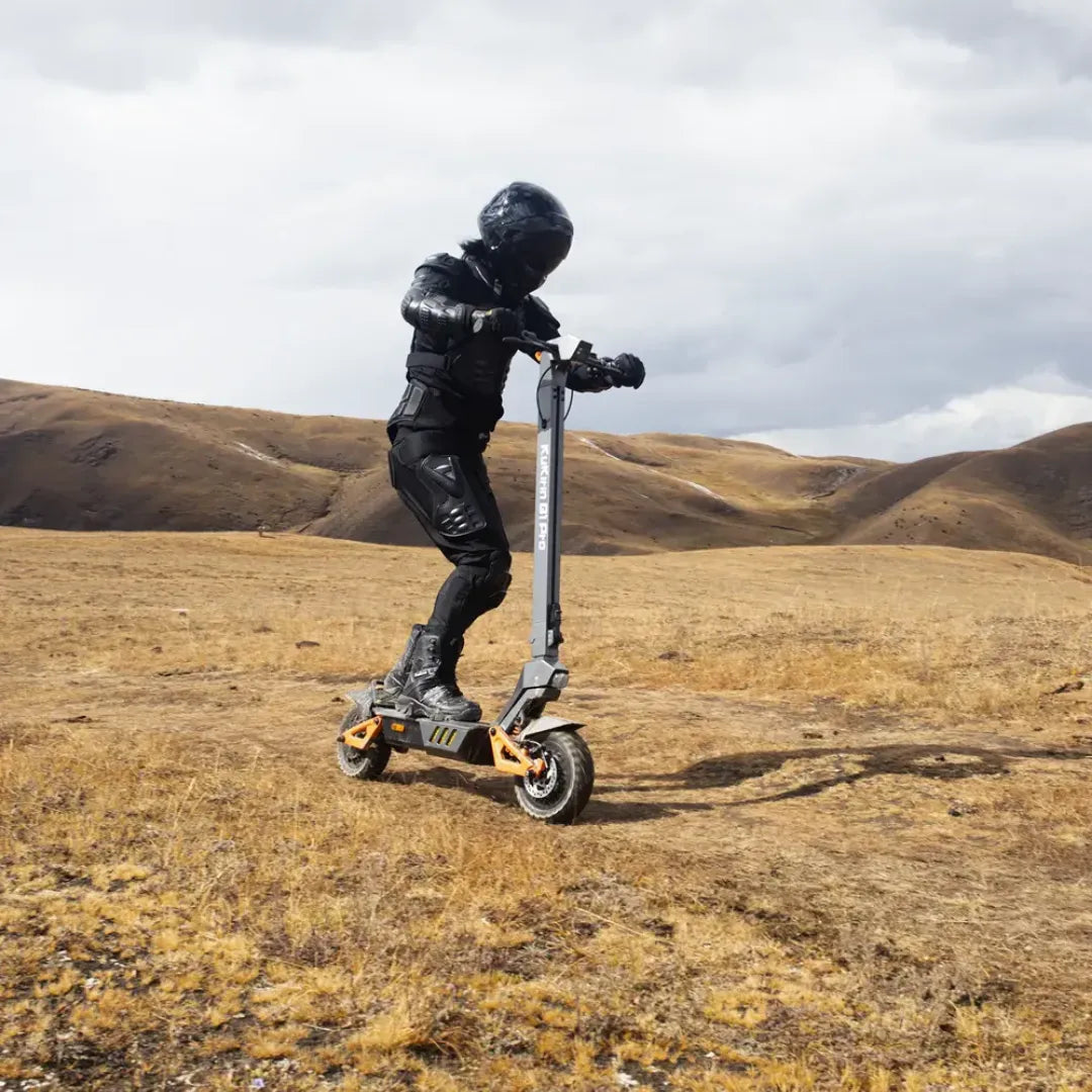 Oseba se vozi z električnim skirojem Kukirin G1 Pro po suhi, travnati pokrajini pod oblačnim nebom.
