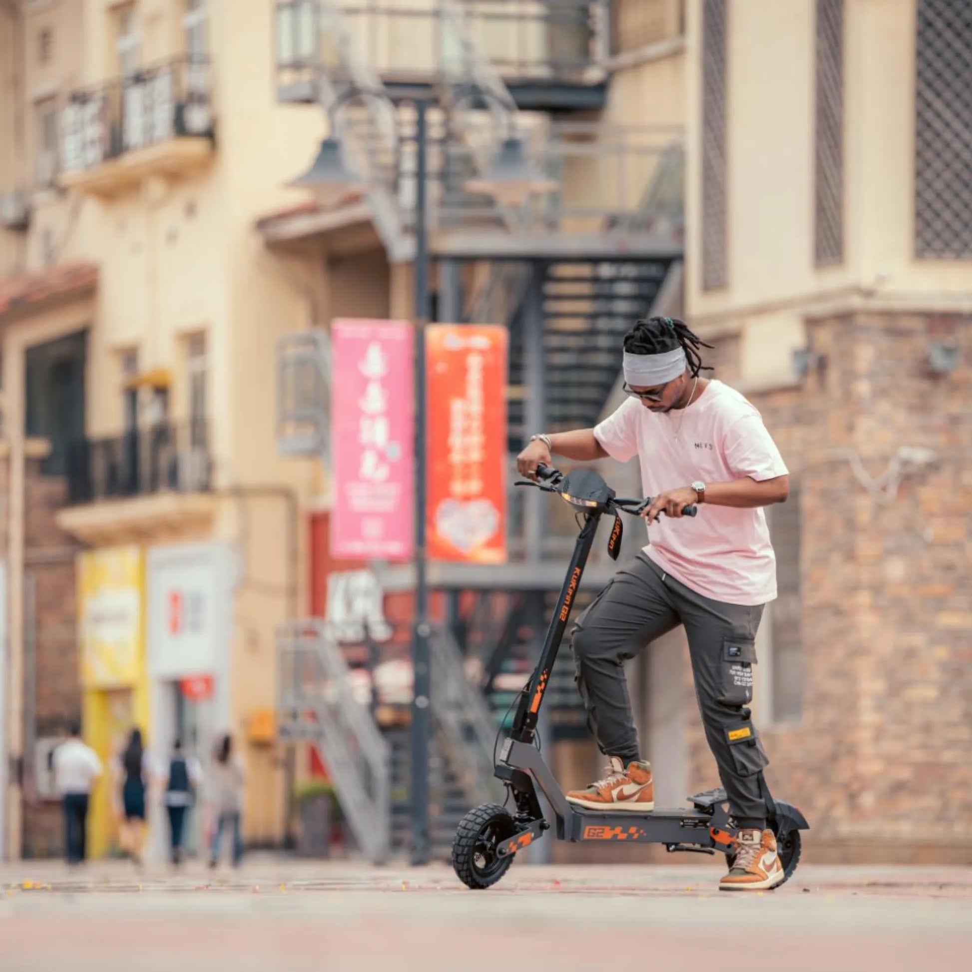 Oseba se vozi z električnim skirojem Kukirin G2 v urbanem okolju s stavbami v ozadju.