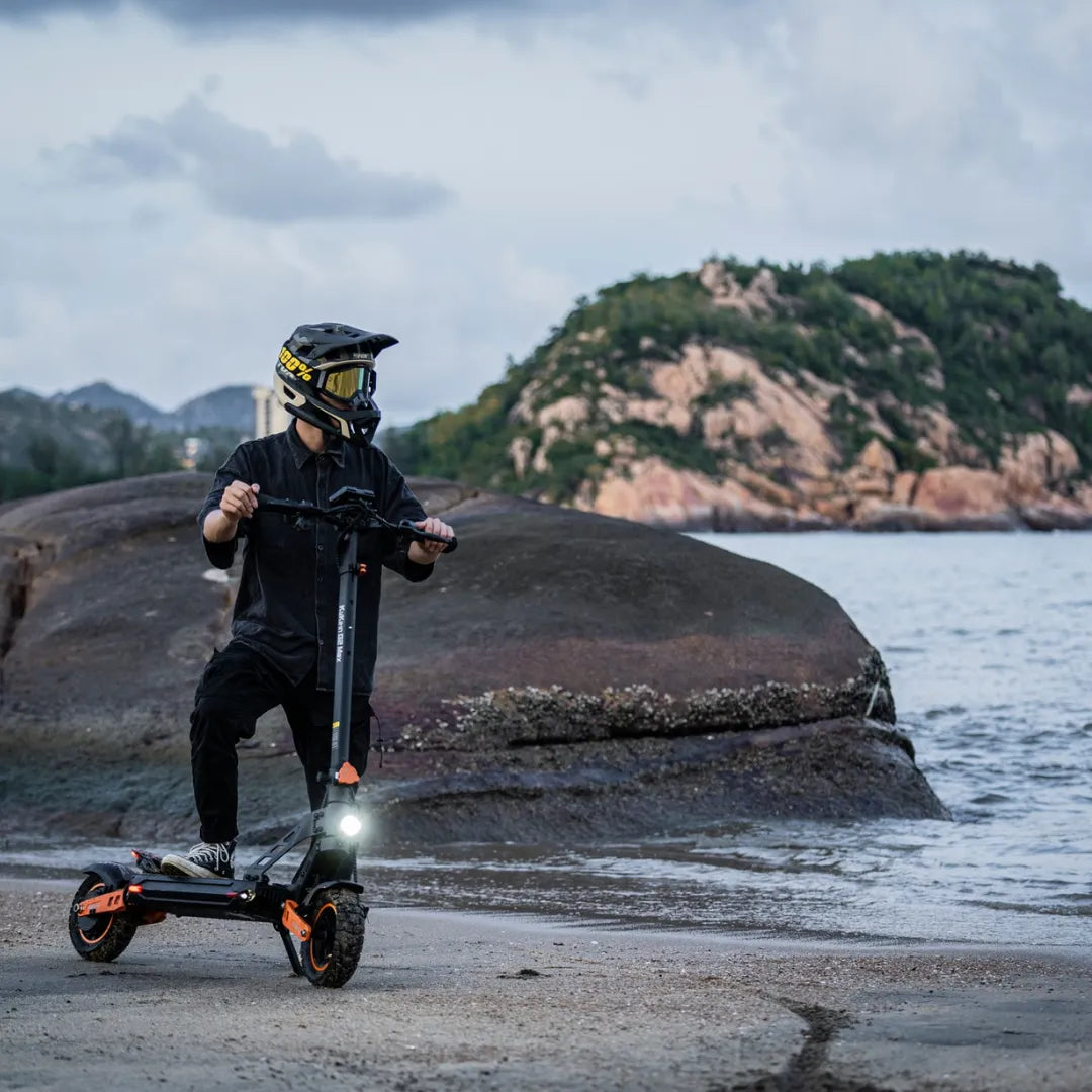 Oseba se vozi z električnim skirojem Kukirin G2 Max ob skalnati obali plaže.